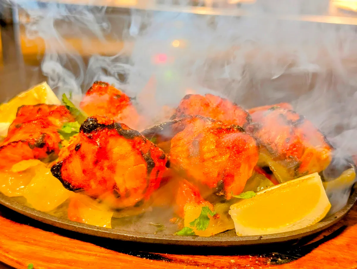 Chicken Tikka Sizzler – Tandoor-marinated chicken tikka arriving dramatically smoking on a sizzling iron plate | SPICE ROOM Denver